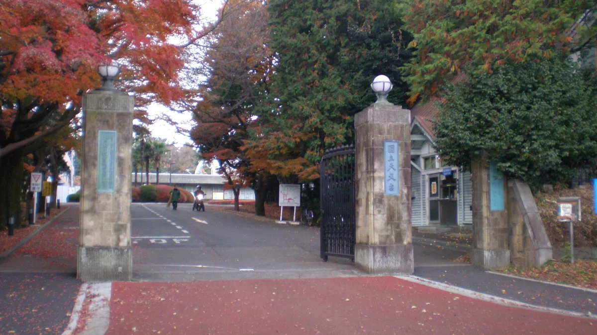紅葉した木々の間にある国立天文台 三鷹キャンパスの正門。石の門柱に施設名の表示がある
