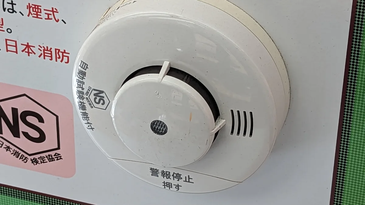 天井に取り付けられた白い円形の住宅用火災警報器。本体に「警報停止 押す」と書かれ、脇に日本消防検定協会のNSマークの表示がある