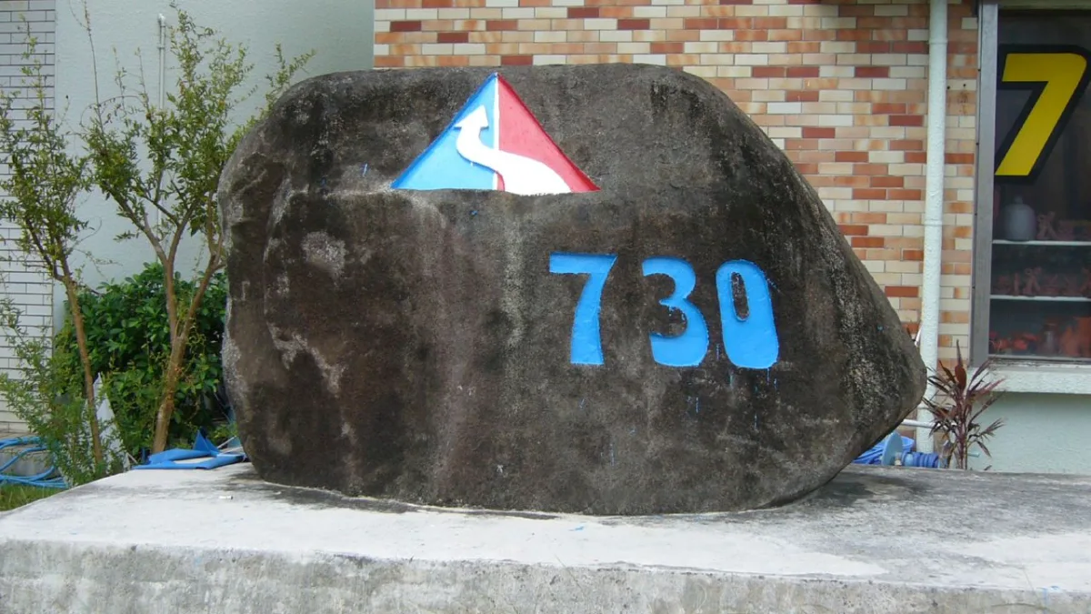 石垣島の交差点に置かれた記念碑。自然石に青色で「730」と大きく刻まれ、上部に矢印を組み合わせた記章がある