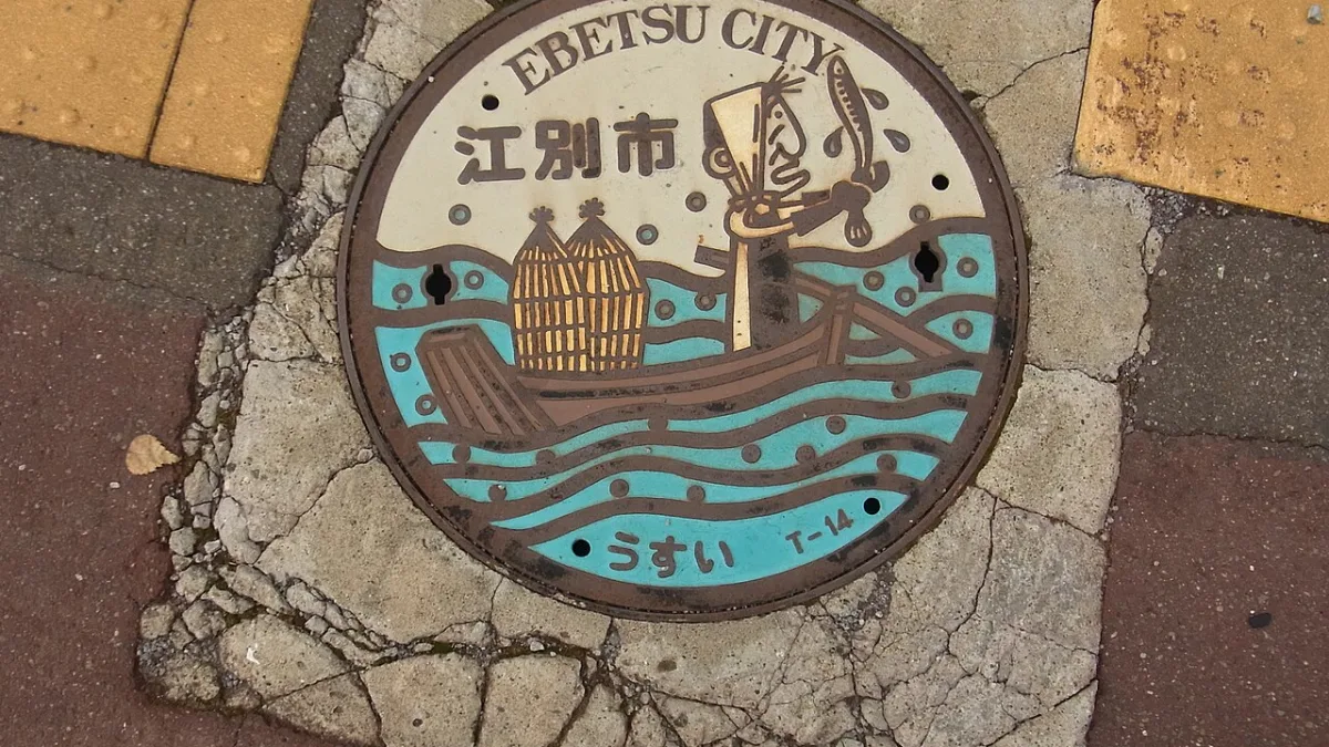 北海道江別市のデザインマンホールふた。円形で、伝統的なヤツメウナギ漁の絵が描かれている