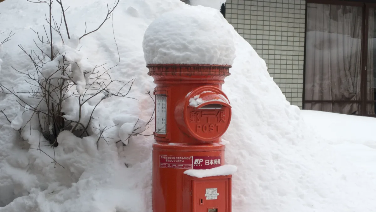 雪に埋もれた街角に立つ、赤い丸型の郵便ポスト。周囲は一面の雪で、赤だけが際立っている